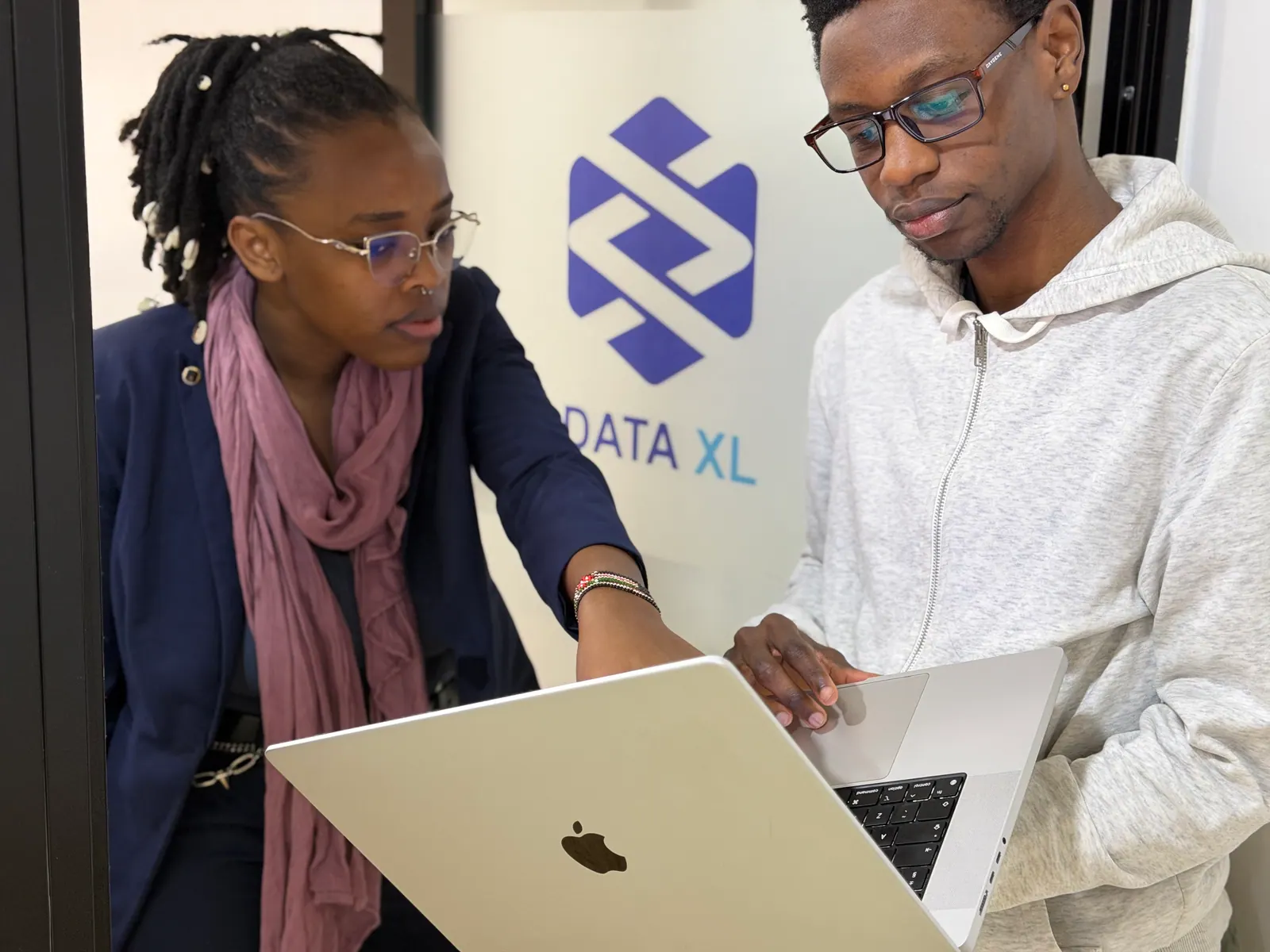 Twee collega's van Data XL bekijken werk op een laptop, met het Data XL-logo op de wand achter hen