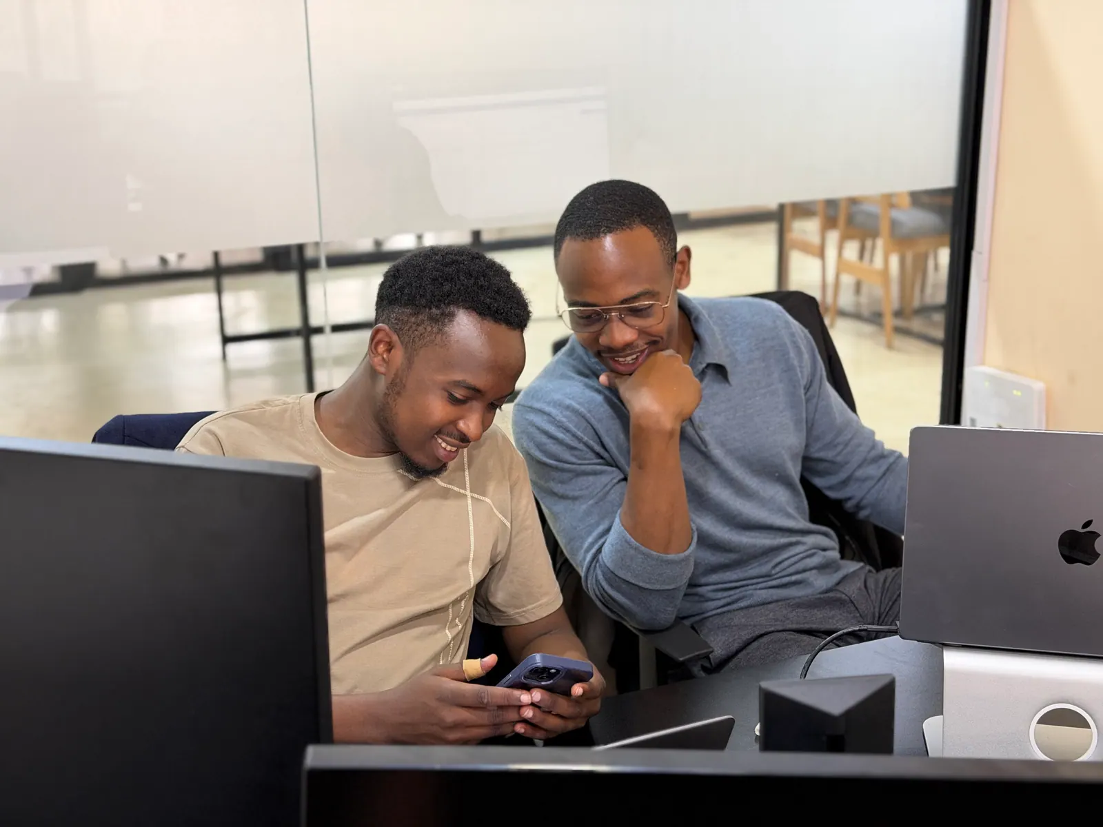 Twee collega's van Data XL aan hun bureau, lachend om iets op een telefoon tussen hen in